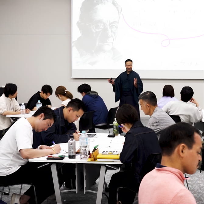 参加者が学ぶテーブルと、前で講義を行う誇高のセミナー風景